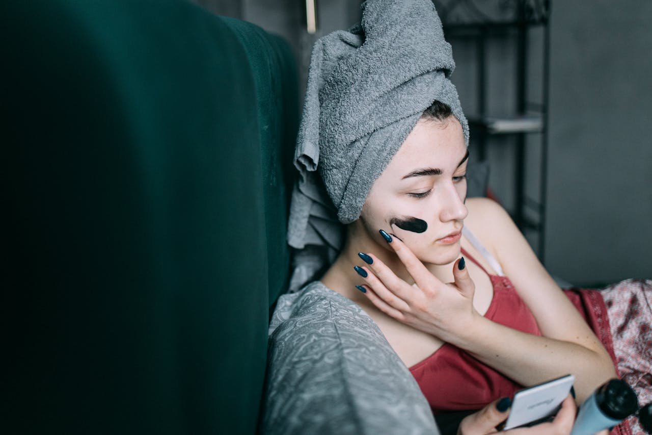 Woman at home applying a facial mask for relaxation and skincare. Self-care routine with a towel on head.